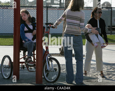 Chelsea (Cq) Fabiszak (Cq), 13, sitzt auf ihrem Fahrrad und blickt über andere genießen die Schaukeln im Sunset View Park in der Nähe von ihrem Haus in Eastlake Freitag, 11. November 2005.  Mutter Veleria (Cq) Fabiszak (Cq) (Mitte, zurück zur Kamera) hält eine Hand auf ihren ältesten und ihre jüngste Tochter, Baby Emmaline (Cq), 10 Mo Stockfoto