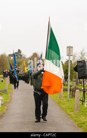 Männer, gekleidet in paramilitärischen Uniformen, und Vertreter der Sinn Féin, der politische Flügel der Irisch-Republikanischen Armee (IRA), halten Sie die Irische trikolore Flaggen während der jährlichen Ostern steigende Gedenken, Belfast, Nordirland. Stockfoto