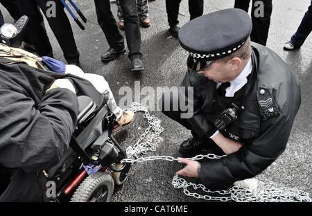 18.04.12, London, UK: ein Polizist entfernt Ketten aus einem Rollstuhl, da Behinderte Demonstranten Straßen am Trafalgar Square auf Fragen eingehen, sie konfrontiert sind, Inclluding Änderungen der Leistungen bei Erwerbsunfähigkeit blockieren. Stockfoto