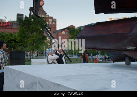 Baltimore, Maryland, USA, 27. April 2012: ein Paar, darunter eine Frau in einem Hijab, auf einem Sockel mit twisted Stahl aus der gefallenen Twin Towers, Teil der Maryland 9/11 Memorial diejenigen, die infolge des 11. September 2001 Angriffe starben ehrt. Die 911 Gedenkstätte, auf einem Platz vor Baltimore's World Trade Center befindet, umfasst auch Kalkstein Artefakte aus dem Pentagon, Granit Monolithen, die auf Flug 93 verloren, und ein Kalkstein Sockel zu den 69 Maryland Opfer der Anschläge. Stockfoto