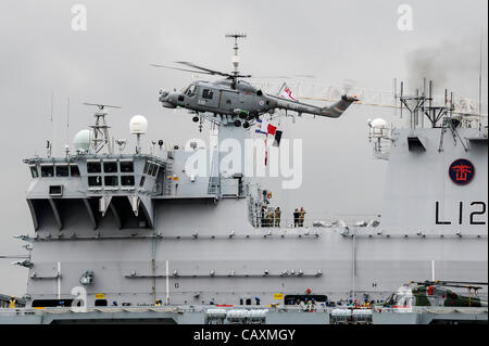 04.05.2012 Themse, London, England. Ein Lynx Hubschrauber kommt auf dem Deck of The Royal Navy Flaggschiff HMS Ocean zu landen, die an ihrem temporären Liegeplatz auf der Themse in Greenwich in London 2012 Olympics Sicherheitsvorbereitungen teilnehmen gesehen werden kann. Stockfoto