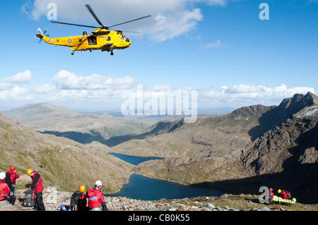 Ein Rettungshubschrauber C Flug 22 Squadron RAF Valley, bereitet sich auf eine verletzte Walker (in trage rechts), Winde von Mount Snowdon, Wales höchste Berg, am 15. Mai.  Freiwillige aus Llanberis, Aberglaslyn & RAF Valley Mountain Rescue Teams (links) befindet sich & trug die verletzte Walker, Sicherheit Stockfoto