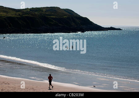 Swansea - UK 22. Mai 2012 - A Jogger und ein paar Paddel-Boarder machen das Beste aus der Sonne bei Langland Bucht heute Morgen. Stockfoto