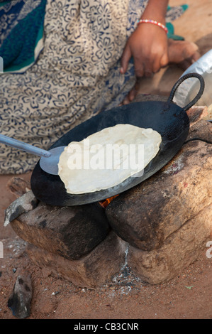 Junge indische Frau in einem ländlichen Dorf Chapati am offenen Feuer vor ihrem Haus machen. Andhra Pradesh, Indien Stockfoto