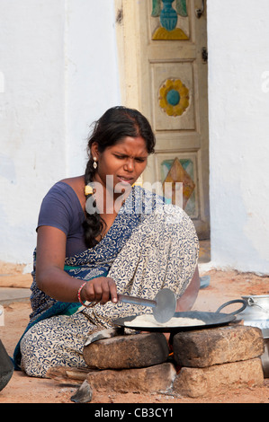 Junge indische Frau in einem ländlichen Dorf Chapati am offenen Feuer vor ihrem Haus machen. Andhra Pradesh, Indien Stockfoto