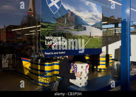 Shopper in Glasgow Zweig des Supermarktes Lidl mit Firmenfarben und Kasse Zähler & Willkommen in Schottland Plakat. Stockfoto