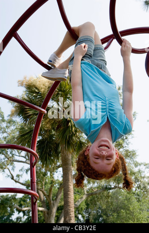 Mädchen hängt kopfüber an Klettergerüst auf einem Spielplatz Stockfoto