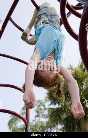 Mädchen hängt kopfüber an Klettergerüst auf einem Spielplatz Stockfoto