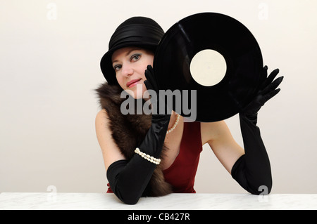Junge schöne Dame in schwarz retro Hut und Handschuhe halten eine Vinyl Record lächelnd Stockfoto