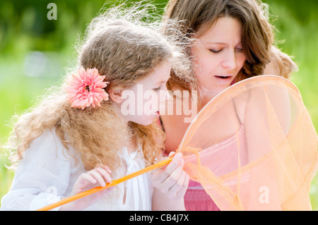 schöne kleine Mädchen und ihre Mutter in das Schmetterlingsnetz suchen. Sommerpark im Hintergrund. Stockfoto