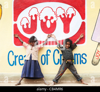 Lächelt glücklich armen indischen nomadischen Bettler Mädchen vor einem Freude Wandbild an der Wand steht. Andhra Pradesh, Indien Stockfoto