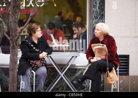 Zwei Frauen sitzen am Bürgersteig Café-Tisch am schwarzen Freitag, während Man Laptop Fenster verwendet. Oak Park, Illinois. Stockfoto