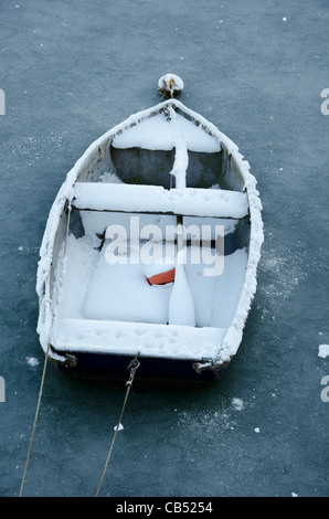 Eine kleine hölzerne Beiboot mit Schnee bedeckt und umgeben von Eis im Hafen von Whitehaven, Cumbria, England. Stockfoto