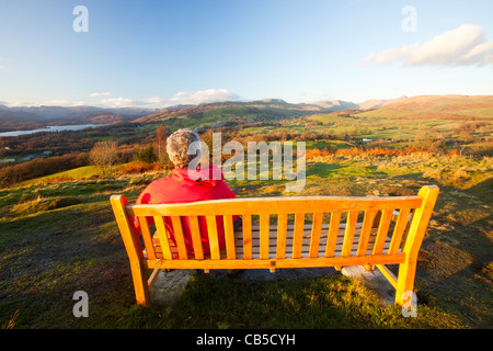 Ein Mann sitzt auf einem Denkmal Sitz auf Orrest Head oben Windermere im Lake District, Cumbria, England. Stockfoto