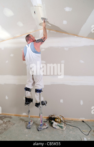 Man plastering wall on stilts Stockfoto