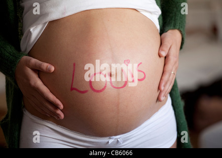 Hautnah auf dem Bauch einer schwangeren Frau mit dem Namen Louis darauf geschrieben. Stockfoto