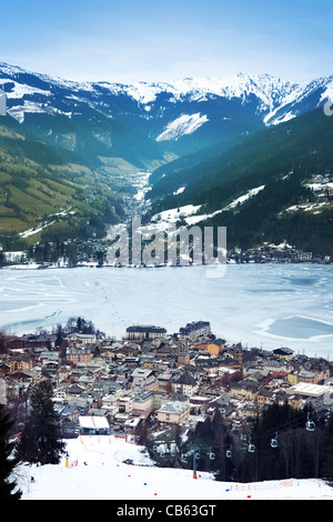 Luftaufnahme unten in Zell Am See (Österreich, Alpes) Stadt, gefrorene See, Skigebiet und Berge im Nebel. Stockfoto