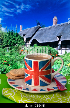 Englischer Tee Union Jack Flagge themed Tasse Tee und Kekse, typische Reetdachhäuser und Garten im Hintergrund UK Stockfoto