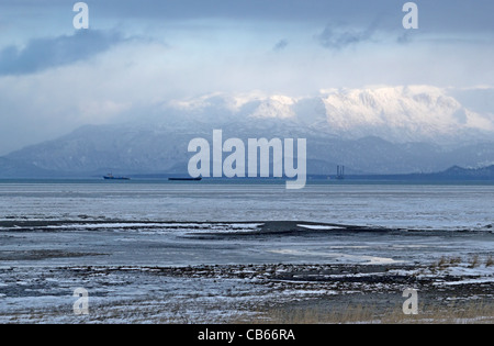 Kenai Mountains erhebt sich über Mud Bay im Winter mit Binnenschiffen und eine Bohrung rig im Hintergrund. Stockfoto