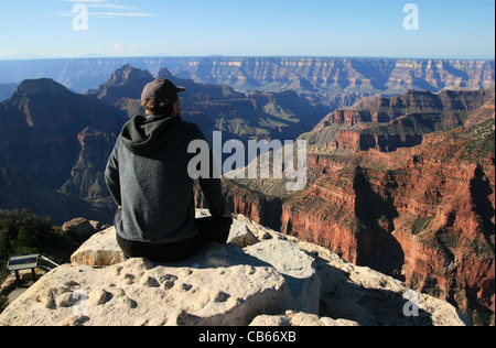 ein Mann sitzt auf einem Felsvorsprung am Bright Angel Point blickt über den North Rim des Grand Canyon, Arizona Stockfoto