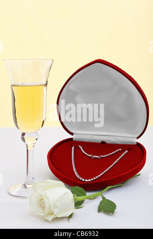 Foto von einer Diamant-Halskette in ein Herz geformt Schmuckschatulle mit einem Glas Champagner und weiße rose. Stockfoto