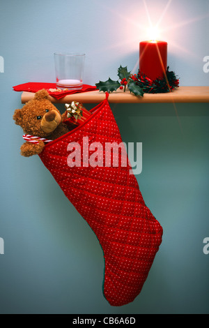 Foto von einem Weihnachts-Strumpf voller Geschenke und eine Kerze, umgeben von Holly, Stockfoto