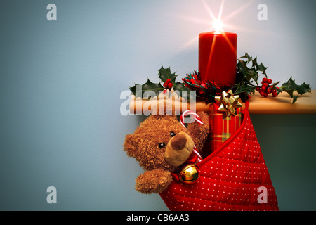 Foto von einem Weihnachts-Strumpf voller Geschenke und eine Kerze, umgeben von holly Stockfoto