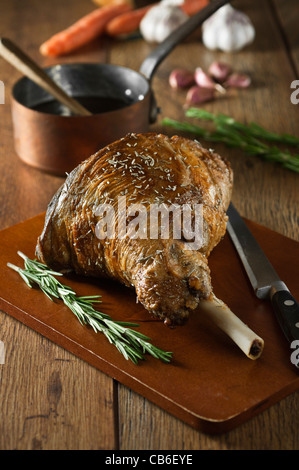 Gebratene Lammkeule mit Knoblauch und Rosmarin auf einem Schneidebrett Stockfoto