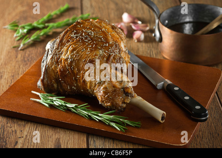 Gebratene Lammkeule mit Knoblauch und Rosmarin auf einem Schneidebrett Stockfoto