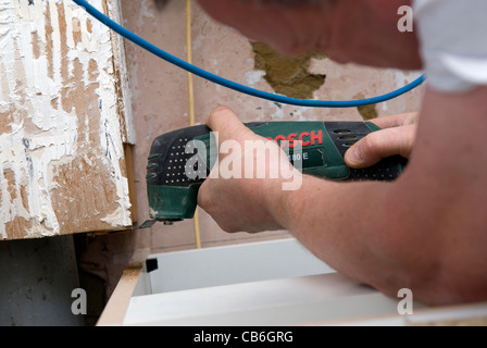 Mit Bosch Werkzeug ausschneiden Rohrstück Kaufmann Surround während der Montage der neuen Küche Installation in Wohnhaus, Bordon, Hampshire, UK. Stockfoto