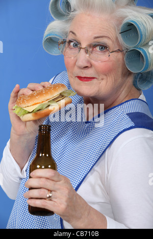 Alte Frau in Rollen mit einen Burger und ein Bier Stockfoto