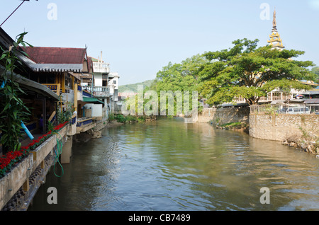 Mae Nam Sai Fluß hat Maesai Thailand links mit roten Blumen gesäumt Gebäude & Tachileik Myanmar rechts mit Bäumen & Pagode Stockfoto