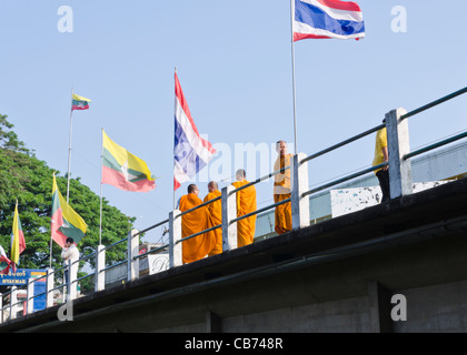 Buddhistische Mönche in orangefarbenen Gewändern zu Fuß über die Brücke zwischen Mae Sai Thailand und Myanmar Tachileik mit Thai & burmesischen Fahnen Stockfoto