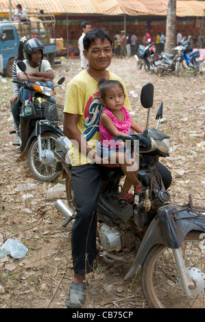 Lächelnder Mann mit seiner Tochter sitzt auf einem Moped bei einem Dorffest, kambodschanischen Neujahr (Chaul Chnam Thmey), Bakong Dorf, Siem Reap, Kambodscha Stockfoto