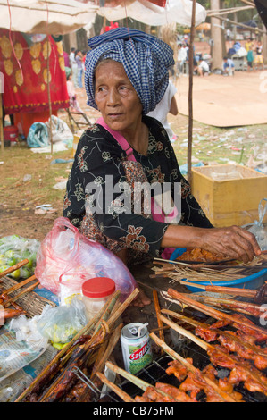 Alte Frau in einem blauen Krama kochen Fleisch Kebab bei einem Dorffest, kambodschanischen Neujahr (Chaul Chnam Thmey), Bakong Dorf, Siem Reap, Kambodscha Stockfoto