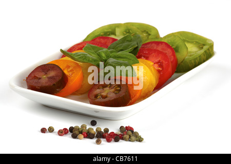 Verschiedene Sorten von Bio Tomatenscheiben auf einem Teller mit Pfefferkörnern isoliert auf weißem Hintergrund Stockfoto