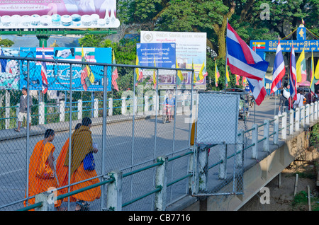 Buddhistische Mönche in orangefarbenen Gewändern Fuß über Brücke zwischen Thailand & Myanmar mit Schild "Republik der Union von Myanmar" Stockfoto