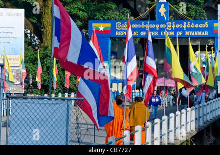 Buddhistische Mönche in orangefarbenen Gewändern Fuß über Brücke zwischen Thailand & Myanmar mit Schild "Republik der Union von Myanmar" Stockfoto