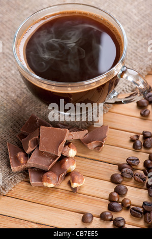 Tasse Kaffee, Schokolade mit Nüssen und Kaffeebohnen auf hölzernen Hintergrund mit Leinwand Stockfoto