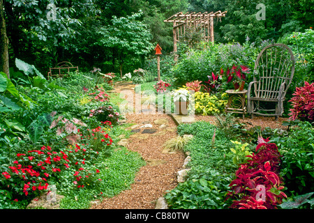 Wunderschön gestalteten Hausgarten mit gebogenen Willow Stuhl, Arbor und eine Vielzahl von Pflanzen und Blumen, Midwest USA Stockfoto