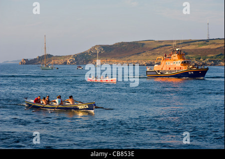 Gig-Rennen auf die Isles of Scilly, Großbritannien mit Rettungsboot in der Ferne. Stockfoto