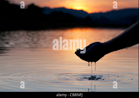 Hohlen Hand raffte Wasser in einem noch See bei Sonnenaufgang in Indien. Silhouette Stockfoto