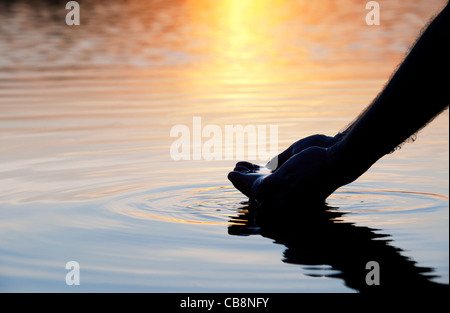 Hohlen Hand raffte Wasser in einem noch See bei Sonnenaufgang in Indien. Silhouette Stockfoto