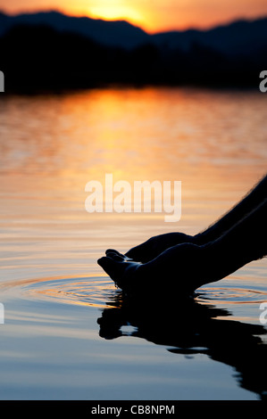 Hohlen Hand raffte Wasser in einem noch See bei Sonnenaufgang in Indien. Silhouette Stockfoto