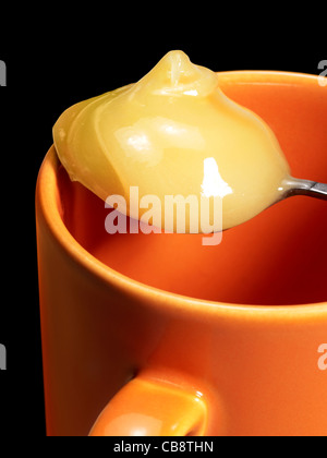 Detail eines Löffels mit cremiger Honig auf eine Tasse. Studio in schwarz Rücken geschossen Stockfoto