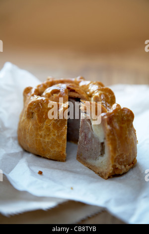 Aufrechte Nahaufnahme der perfekte Schweinefleisch-Torte mit einer Scheibe auf der Papierverpackung auf einer hölzernen Tischplatte ausschneiden. Stockfoto