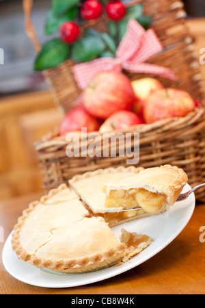 Apfelkuchen auf einem Holztisch mit einem Korb voller Äpfel im Hintergrund Stockfoto