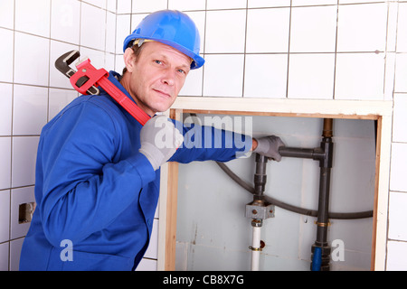 Erfahrenen Klempner mit einem großen Schraubenschlüssel in einem Badezimmer Stockfoto