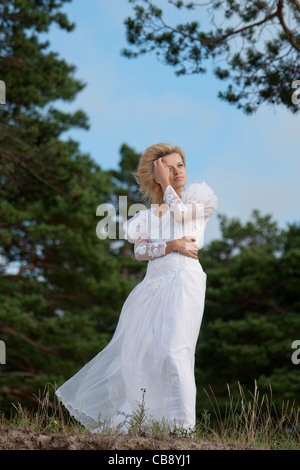 Frau steht auf einer Klippe in einem langen weißen Kleid und Blick in den Horizont Stockfoto