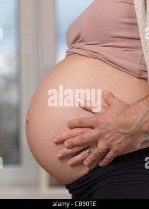 Nahaufnahme eines Ehemannes hält seine Hände um seine schwangere Frau Bauch Stockfoto